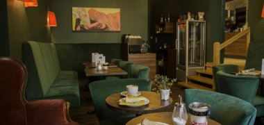 Das Scala Cafe Das Scala Cafe dekoriert mit grünen Sitzmöbeln. Auf den Tischen stehen Kaffee und Kuchen
