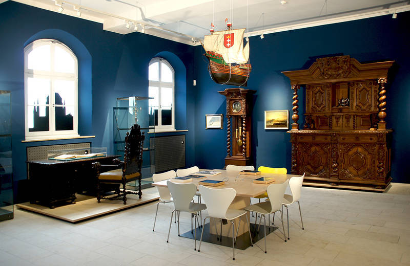 Ein Raum mit blauen Tapeten und alten Möbelstücken dekoriert. Von der Decke hängt ein beleuchtetes Segelschiff