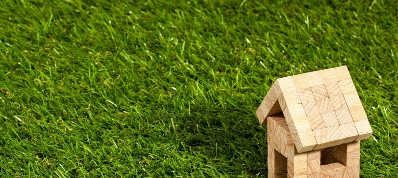 Symbolhaus auf Rasenfläche ein Holzhaus aus Bauklötzen auf einer Rasenfläche