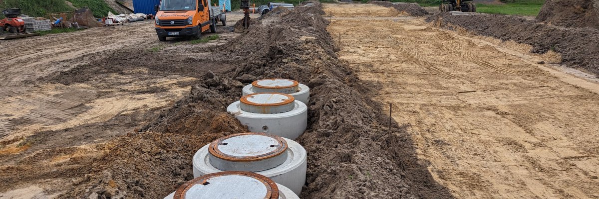 Tiefbauarbeiten im Baugebiet Weidkamp Ein Feld auf dem Erdarbeiten stattfinden. Im Fokus sind mehrere Schächte, die noch nicht bis zur Krone angefüllt sind. Im Hintergrund sind Baustellenfahrzeuge zu erkennen.